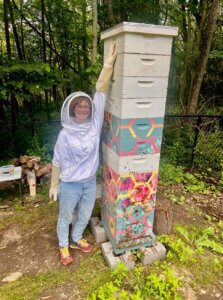 Audrey poses next to her beehive with her arm stretched up to reach the top of the 10 brood box stack.