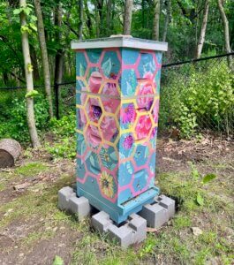 Beehive of five brood boxes, painted blue with bright pink flowers and an overlaying hexagonal pattern.