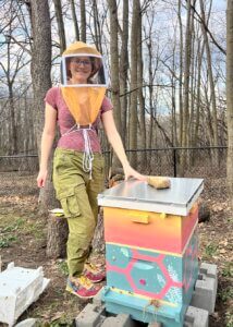 Audrey poses next to her beehive: two brood boxes painted bright colors.