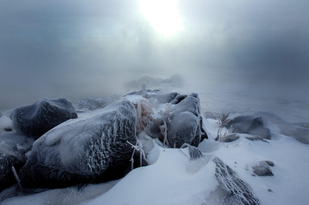 rocks covered in snow and ice, surrounded by fog, with sun in distance