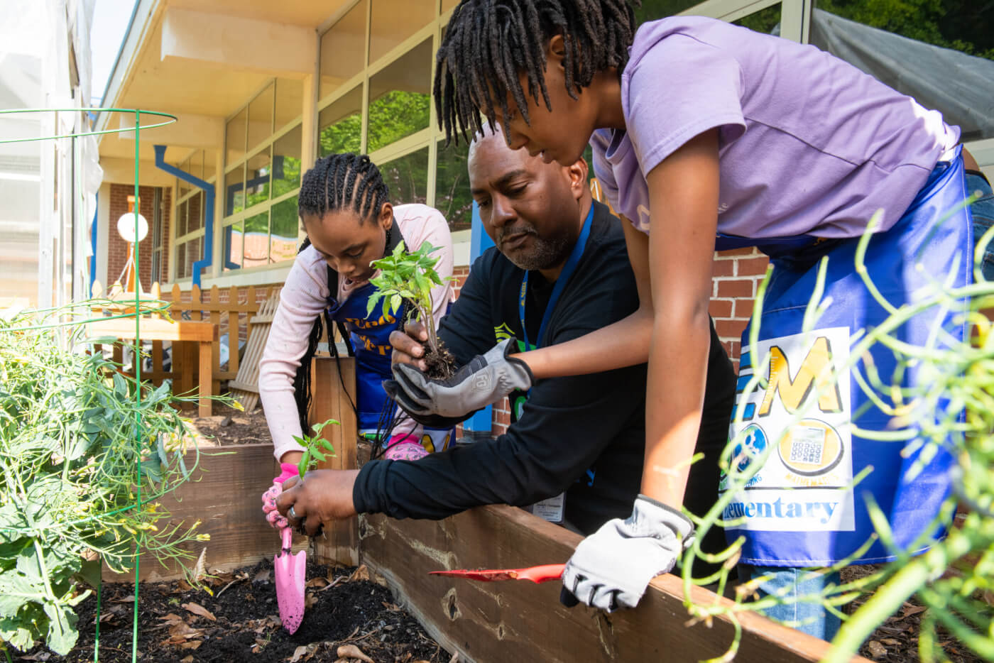 A teacher works with two students in a raised garden bed.