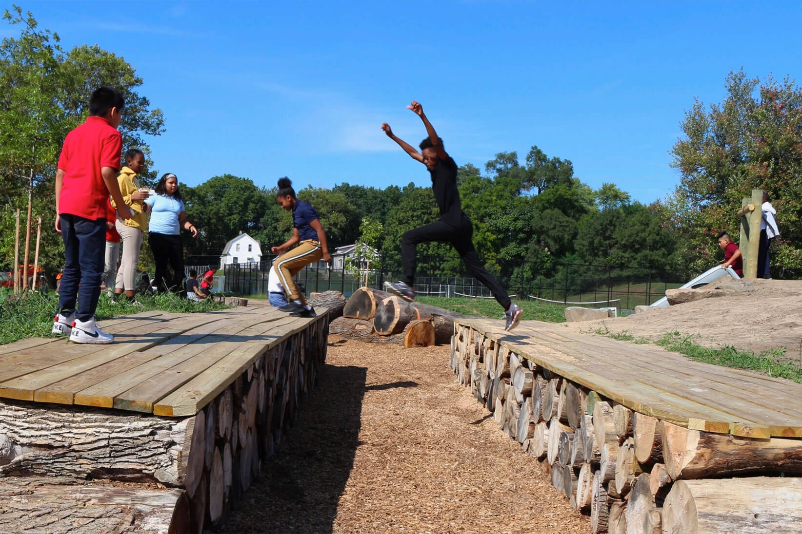 Young and older children jumping over wooden areas.