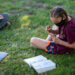 Young girl sitting cross-legged in grass working with a book and notepad.