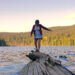 person walking on log on a lake