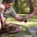 father holding one child and helping another pour water in a bucket