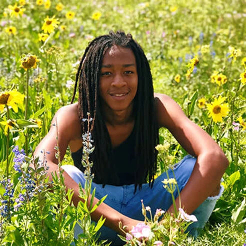 Black boy smiling and sitting in a green field with daisies