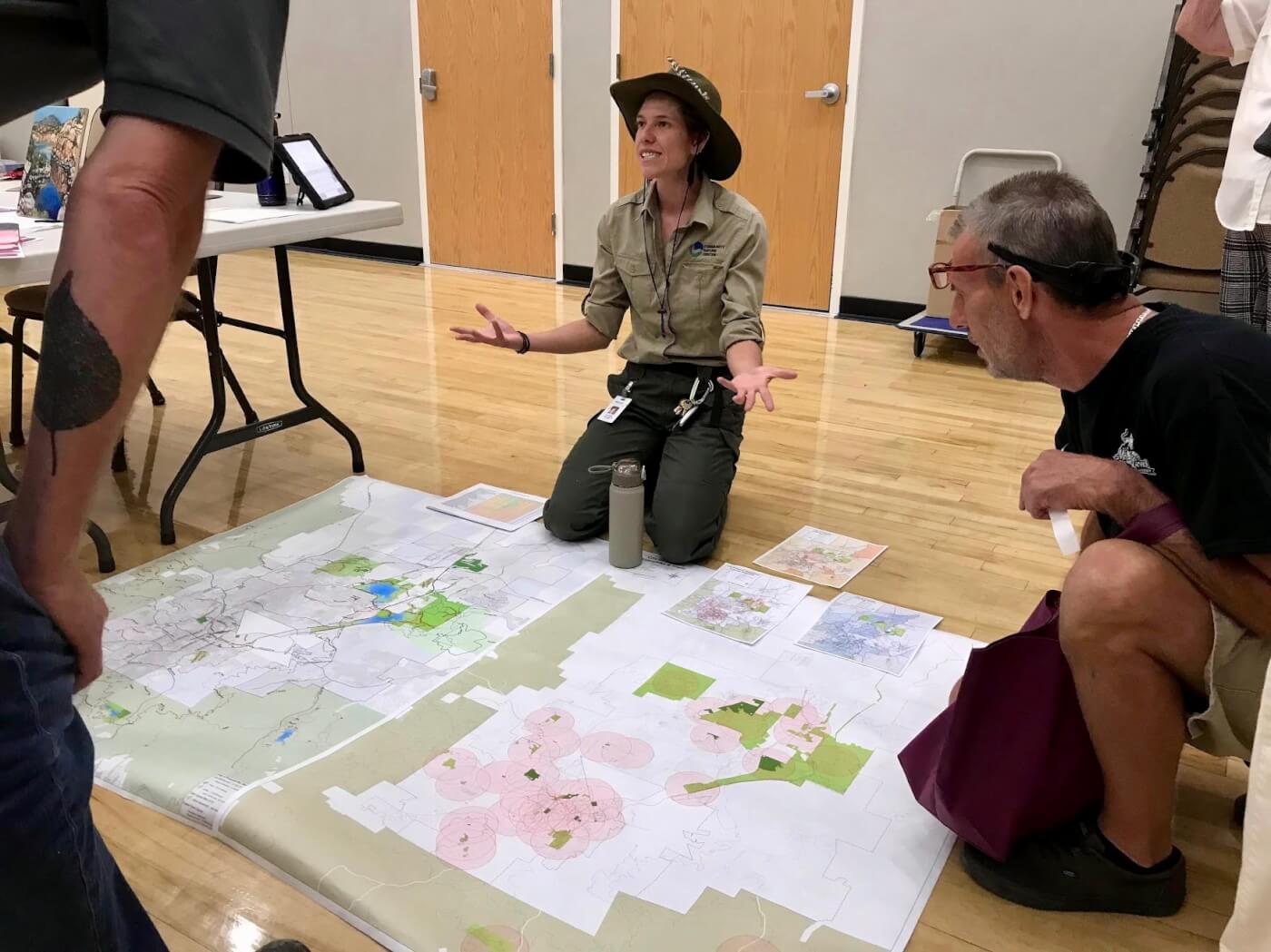 Nature leader sitting on the floor with a variety of papers and posters in front of her with her hand up in the air as she explains something