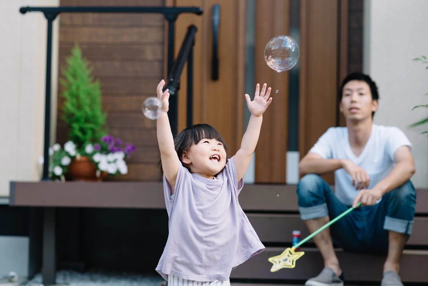 child playing with bubbles and father sitting nearby watching