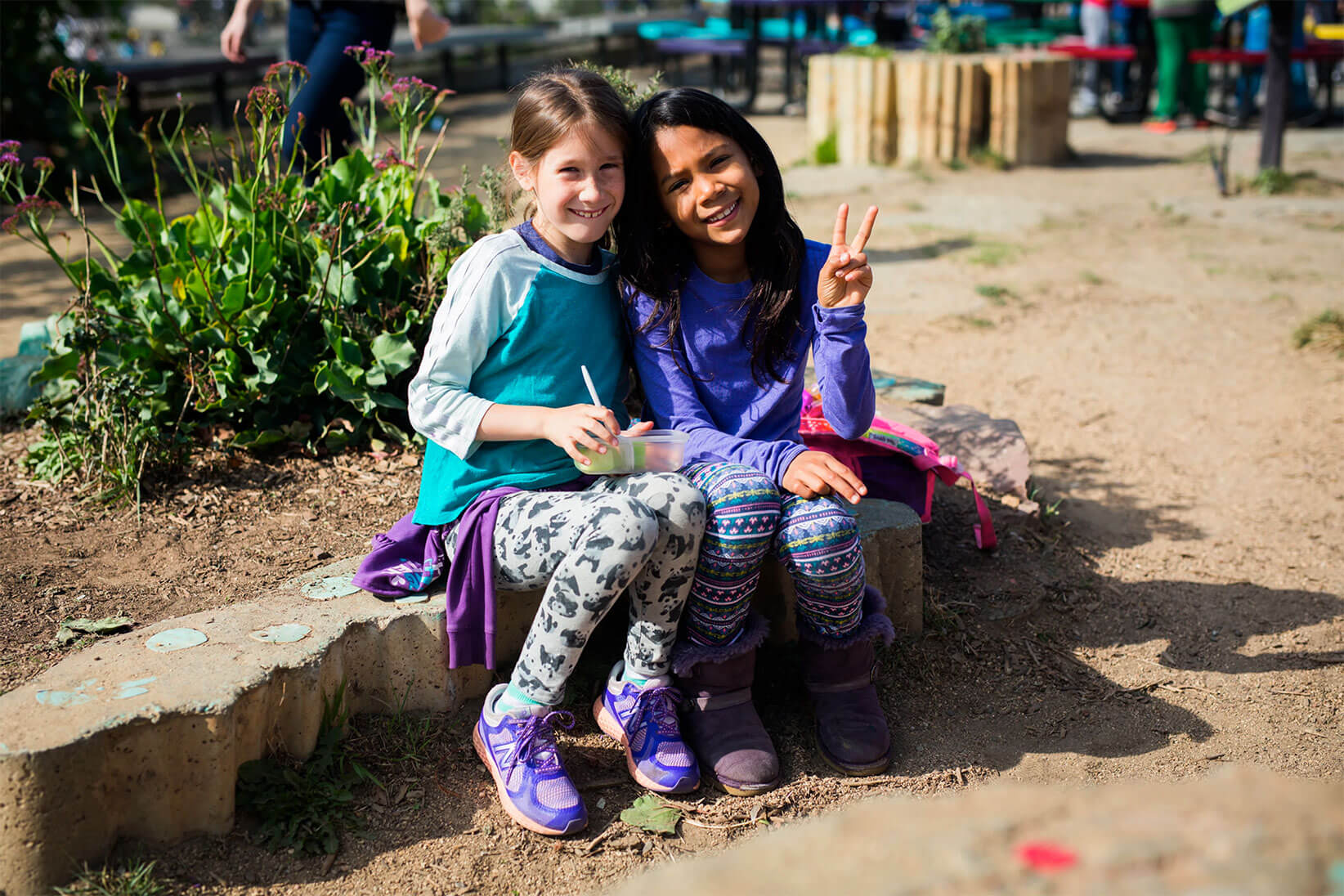 Two girls sitting down on a rock bench smiling and posing for the camera.