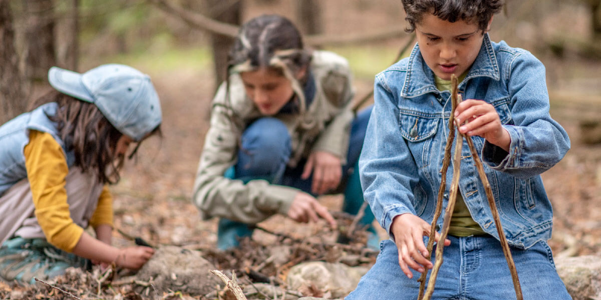 Kids playing outside with sticks and tree branches.