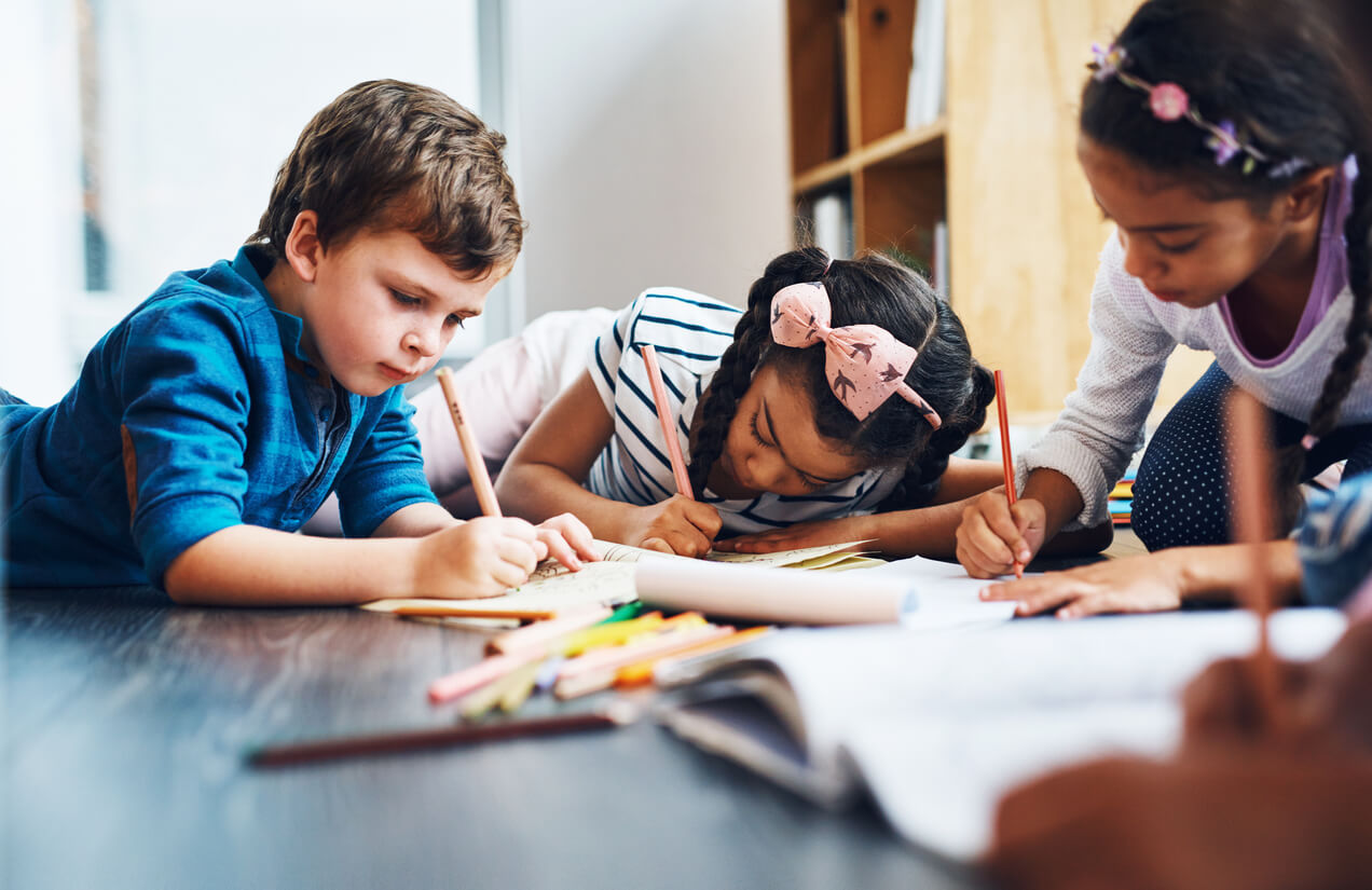 group of kids color on the floor, focused on their art, with pencils in their hand