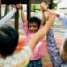 group of elementary school children standing in a circle holding hands raised in the air