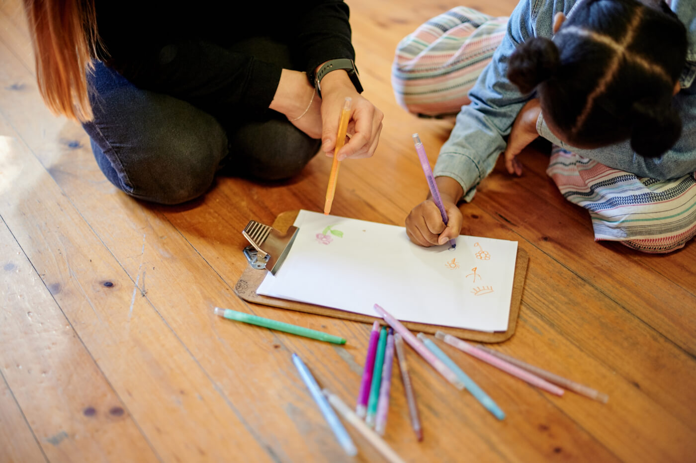 child and adult sitting on the floor while the child drawls with markers