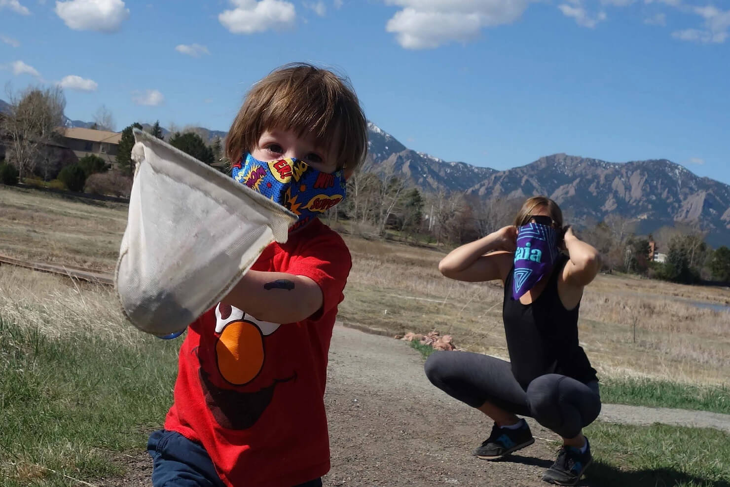 kid with mask holding a net and mother with mask crouching in the back