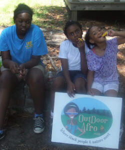Young girls posing with Outdoor Afro sign.